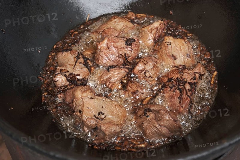 Meat and onions in cauldron. The making of pilaf