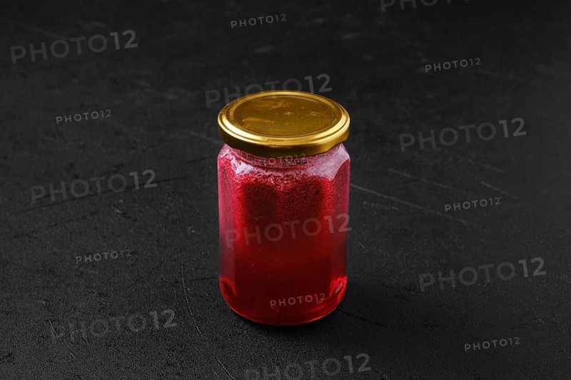 Whole closed jar of cherry jam on black background