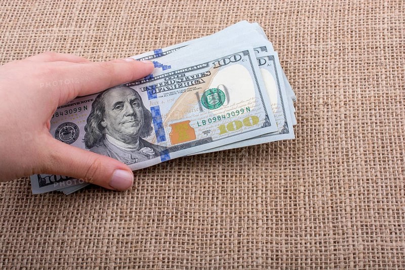 Hand holding banknote bundle of US dollar on a linen canvas background
