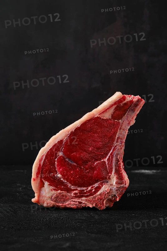 Raw rib-eye steak bone in on dark background closeup