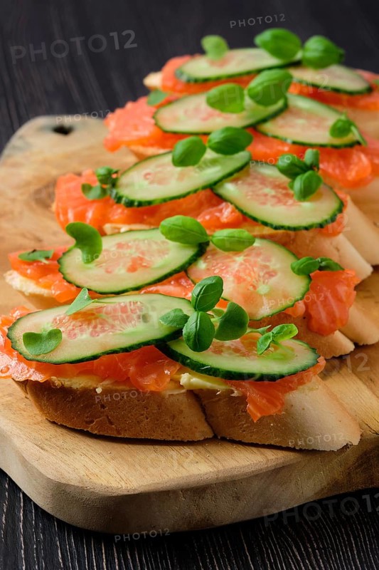 Sandwich with salmon on wooden plate on dark wooden table