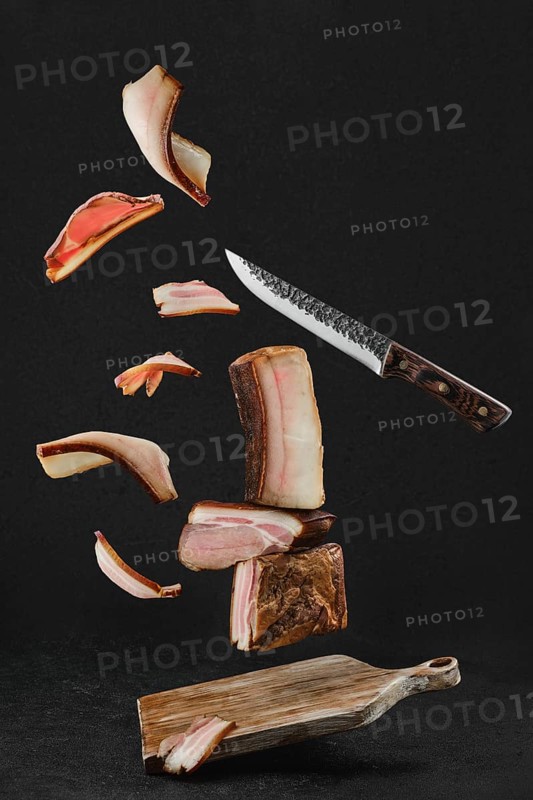 Levitating slices of different smoked pork bacon and lard on wooden cutting board