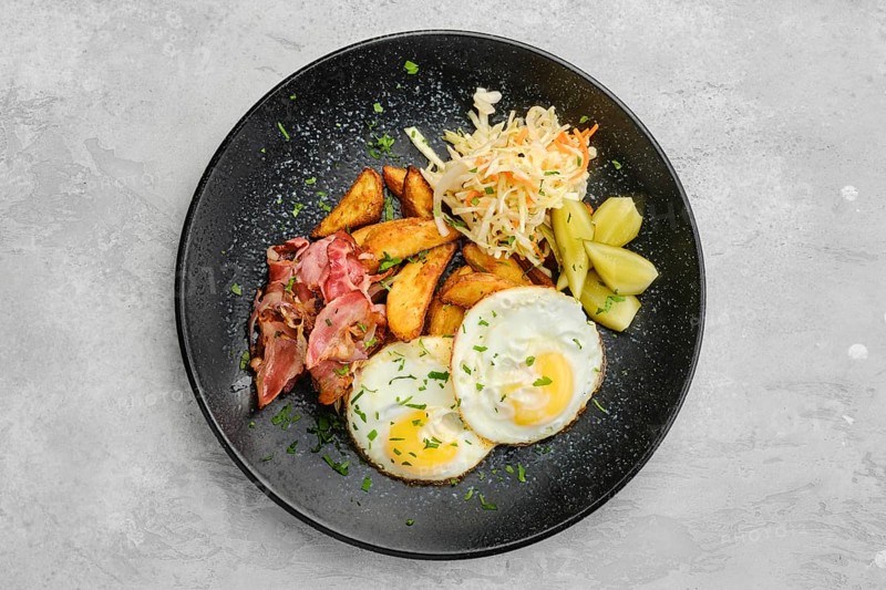 Top view of two fried eggs with bacon and pickled cabbage with cucumber