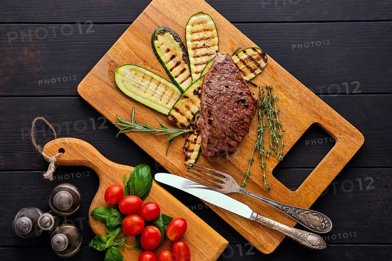 Top view of beef steak and zucchini served with fresh tomato cherry and basil on wooden cutting board