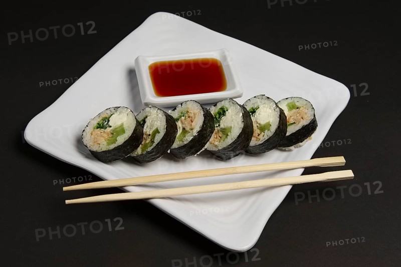 Angle view of portion of chicken teriyaki rolls served on black paper with soy sauce and hashi