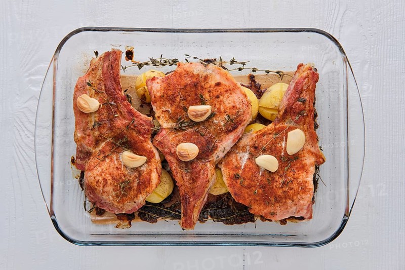 Steak with bone and potato baked in oven in a roasting pan with garlic and thyme