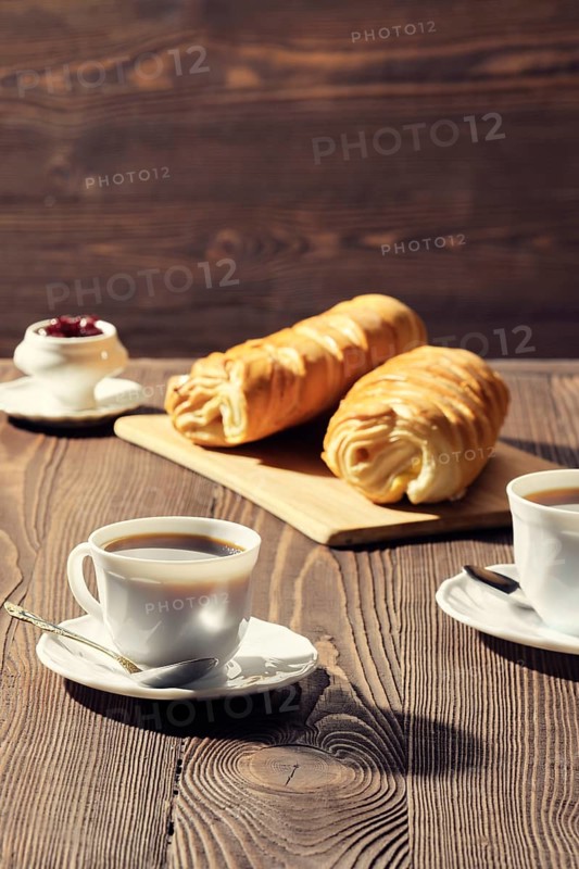 Rolled buns and coffee on wooden table in morning sunlight. Photo with shallow depth of field