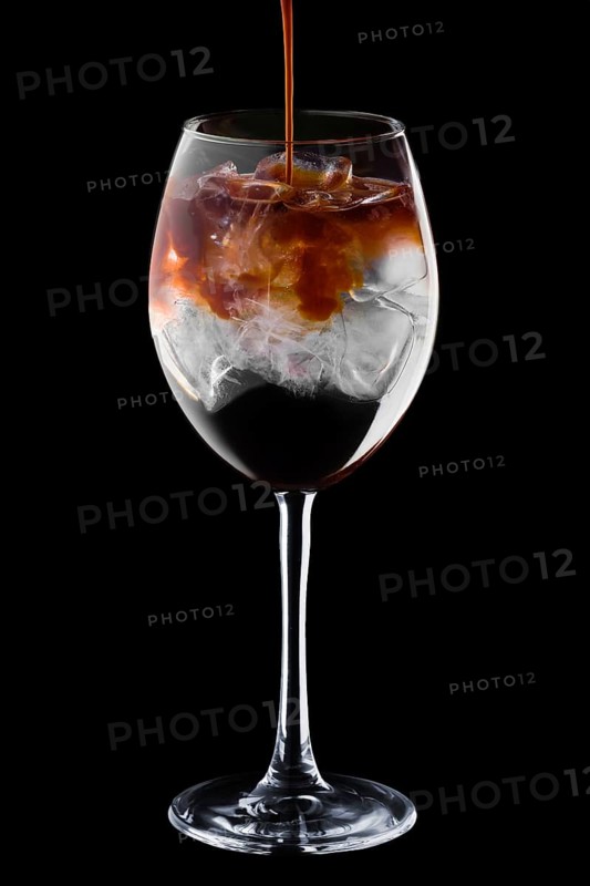 Pouring spresso in cocktail with tonic in wine glass isolated on black background