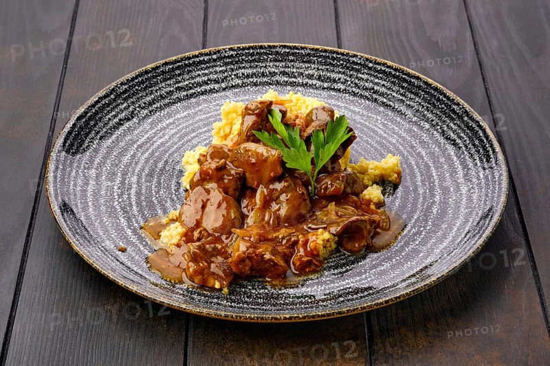 Beef goulash with millet porridge and creamy sauce on dark wooden table