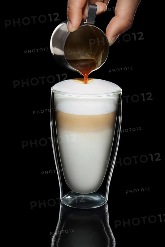 Hand with pitcher making pattern on cappiccino topping
