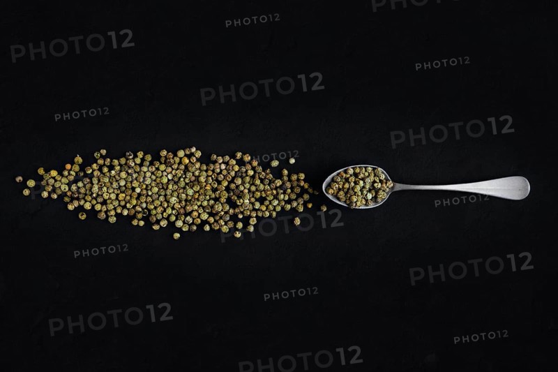 Dry green pepper scattered near metal spoon on dark background
