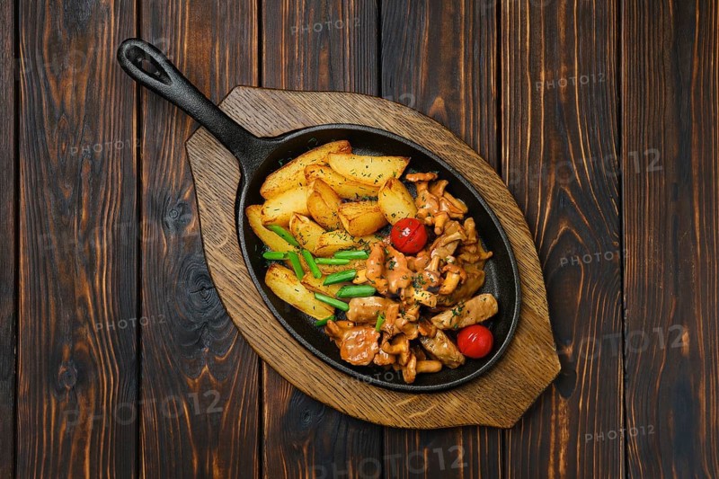 Top view of potato wedges with chanterelles and pork in cast iron skillet