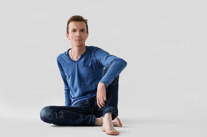 Portrait of middle aged man in blue longsleeve and jeans sitting on the floor with bare feet