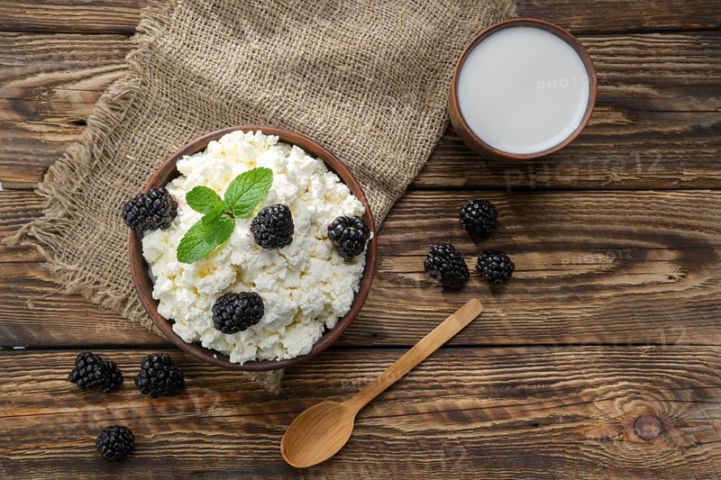 Dairy product cottage cheese and milk in brown ceramic bowl with spoon on wooden table