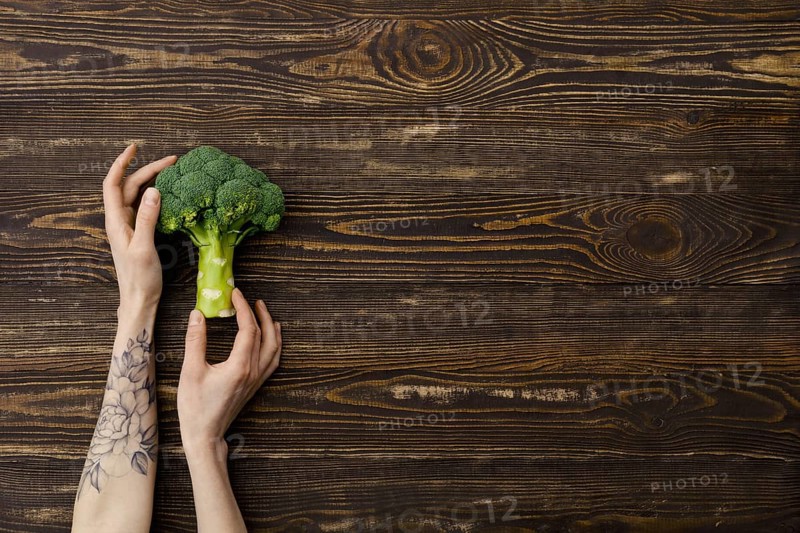 Overhead view of fresh broccoli in hands over wooden background