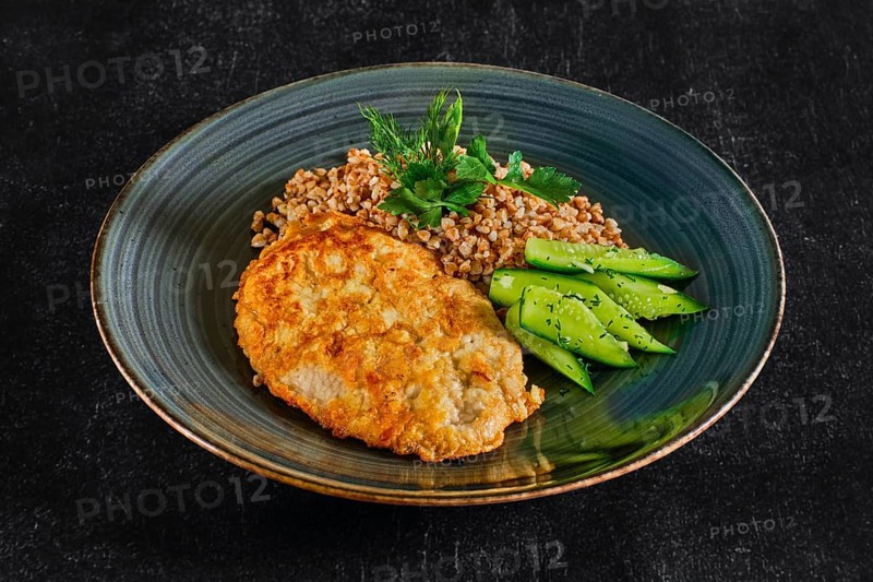 Top view of chicken fillet fried in batter with buckwheat porridge and pickled cucumber