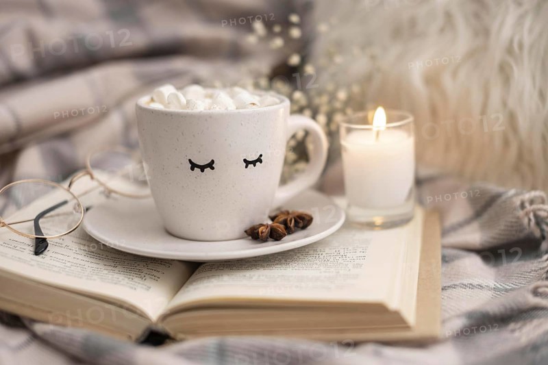 Cup of hot cocoa with marshmallows on book with candle