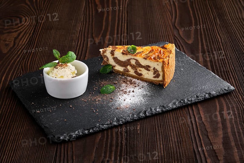 Layered cheesecake with ice cream served on slate plate on dark wooden background