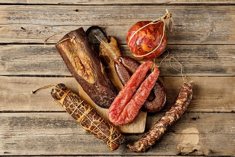 Top view of assortment of dried meat and sausages on wooden background