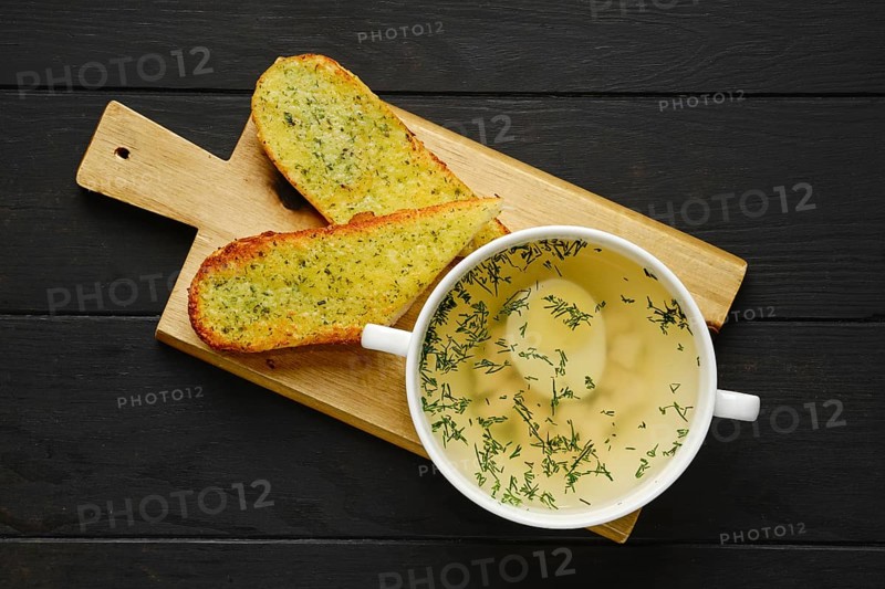 Top view of chicken stock with egg and crispy garlic toasted bread on wooden serving board