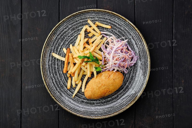 Top view of Kiev cutlet with american fries and red cabbage with carrot as a garnish