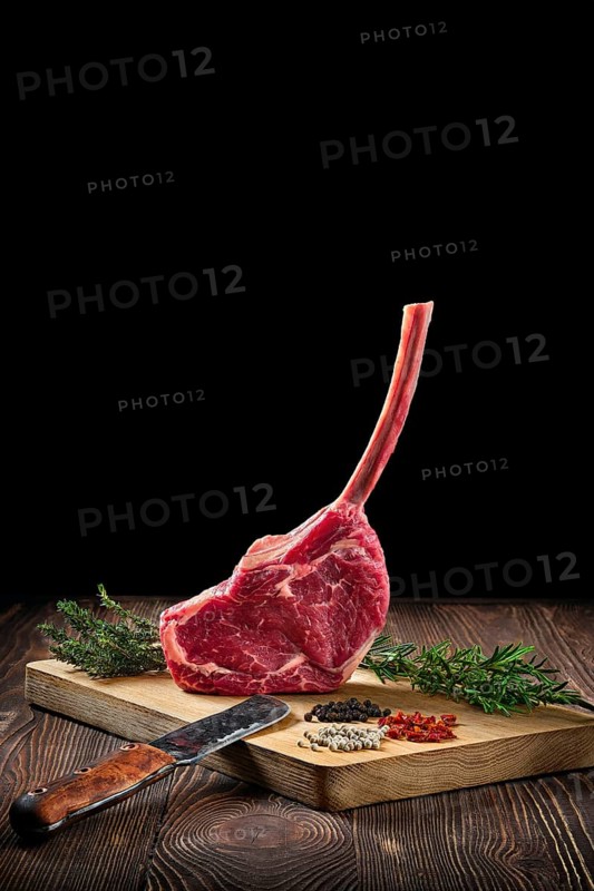 Raw juicy cowboy steak on wooden cutting board with spice