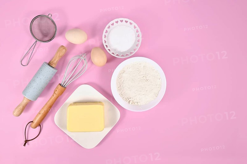 Cake dough ingredients and baking tools on pink background with copy space