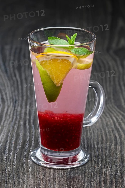 Tall transparent glass with raspberry and citrus tea on dark wooden table