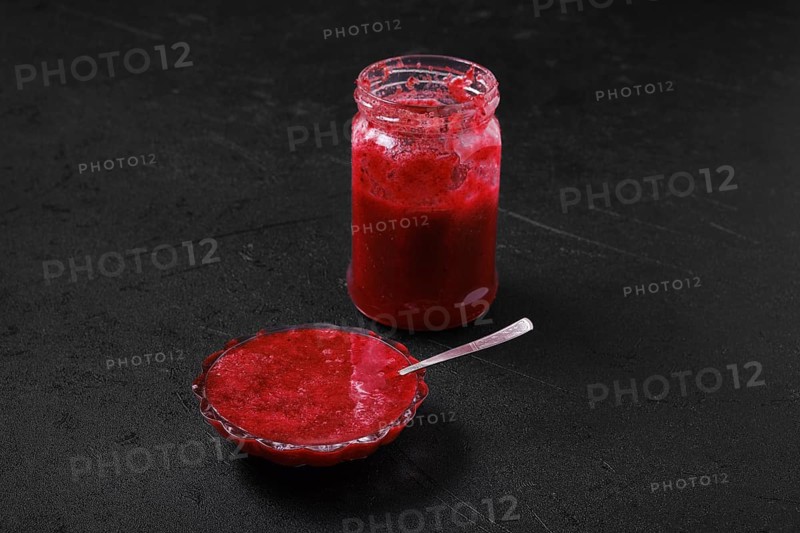 Jar and saucer with cherry jam on black background