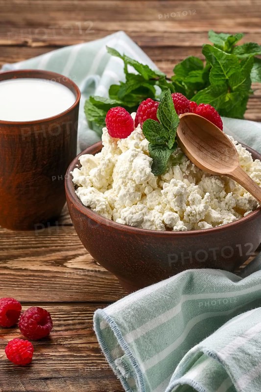 Cottage cheese with wooden spoon on it and milk in clayware on wooden table