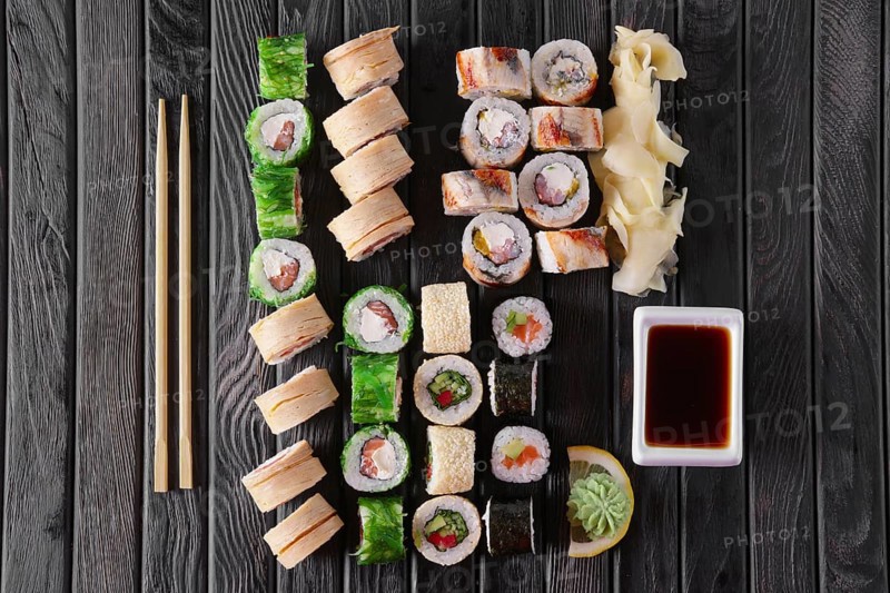 Large set of rolls with garnish and hashi on wooden plate