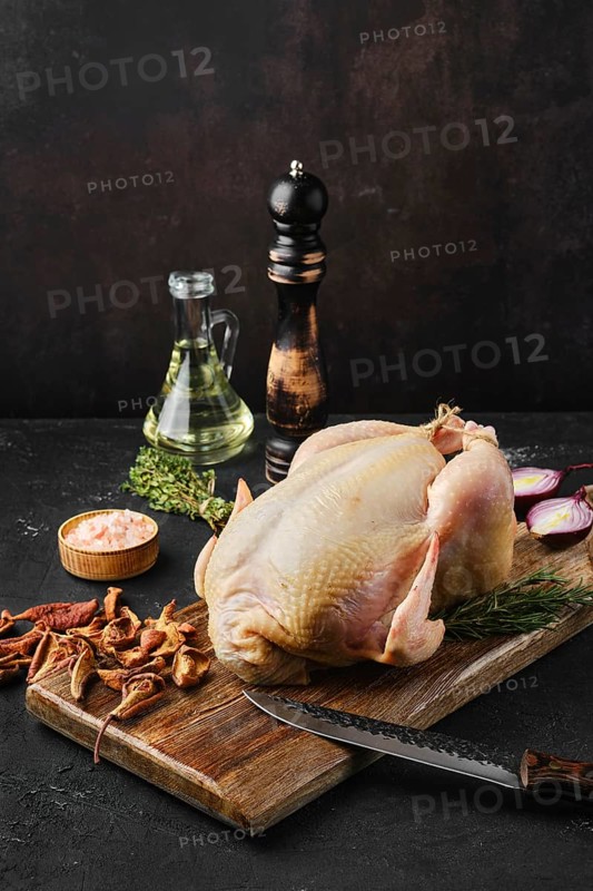 Raw whole broiler chicken with spices on wooden cutting board