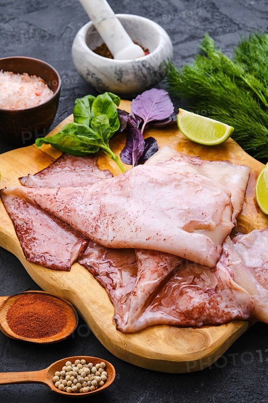 Raw fresh unpeeled squid on wooden cutting board with spice and herbs