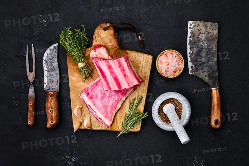 Fresh raw lamb breast ribs on wooden cutting board with herbs and seasoning