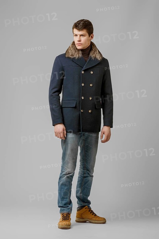Full length portrait of handsome man in warm coat with hood posing in studio