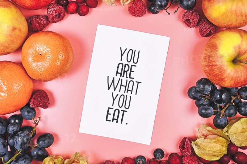 Healthy eating concept with You are what you eat card on pink background surrounded by fruits like apples