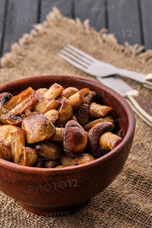 Clay plate with roasted mushrooms on dark wooden table