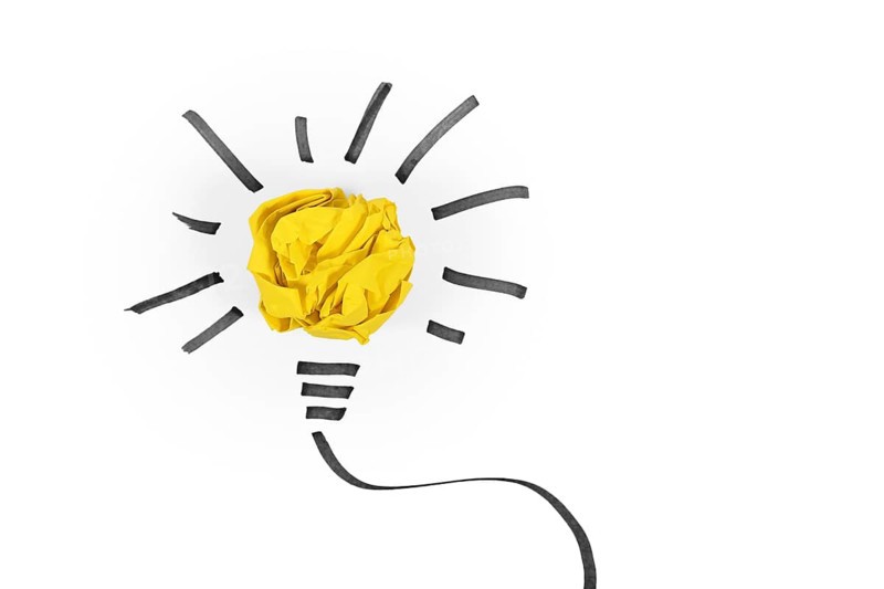 Idea concept with light bulb made out of yellow crumbled paper ball and drawn black lines on white background