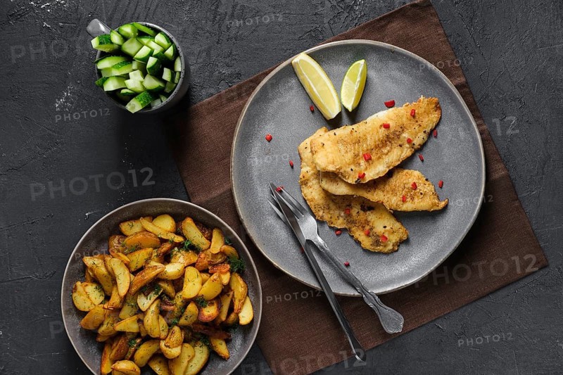 Top view of fried breaded hake fillet with spice and roasted potato wedges