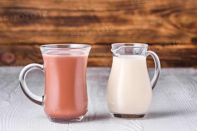 Chocolate milk and soy milk in glass on white table over dark wooden background