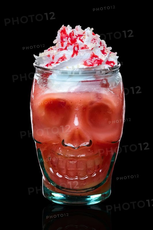 Halloween strawberry cocktail with whipped cream in skull glass isolated on black