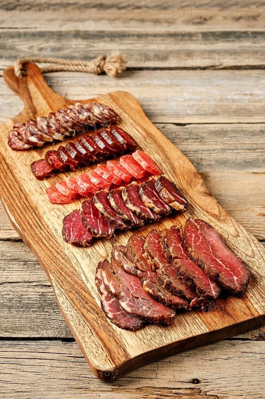 Slices of smoked dried beef and pork meat on wooden cutting board