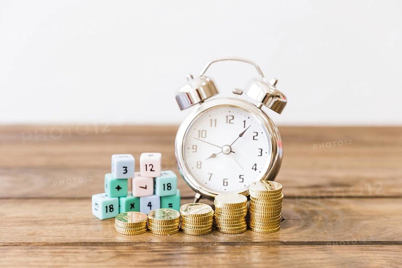 Close up stacked coins front alarm clock math blocks wooden desk
