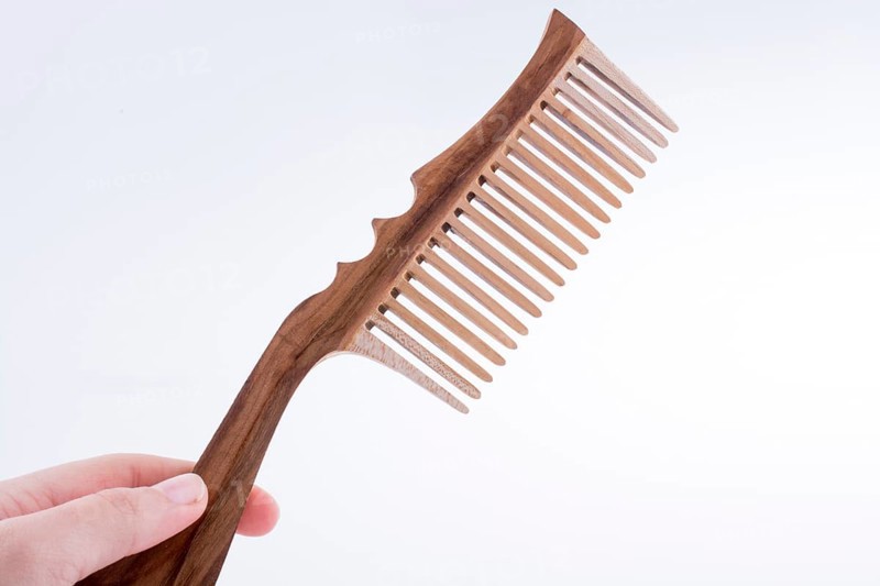 Hand holding a wooden hair comb on a white background