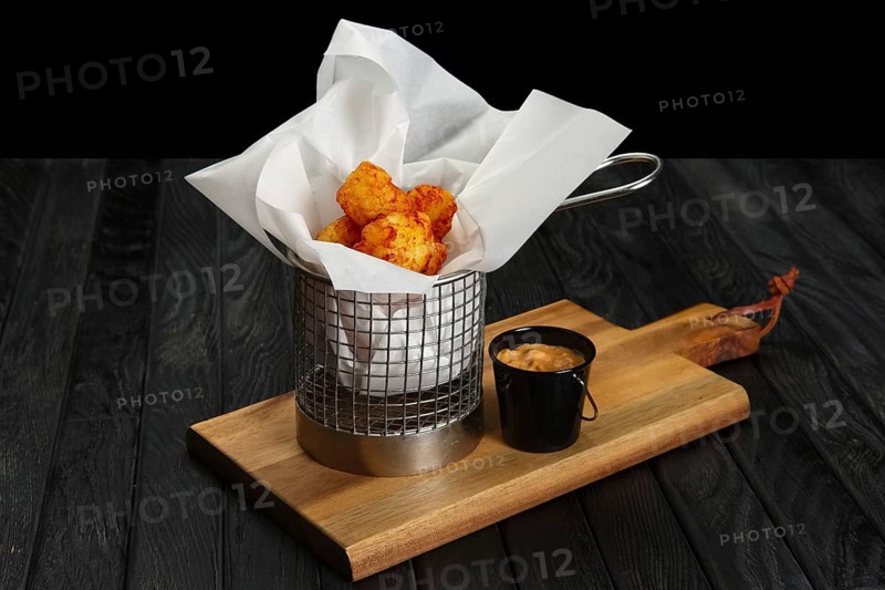 Deep fried potato balls in metal basket on wooden board