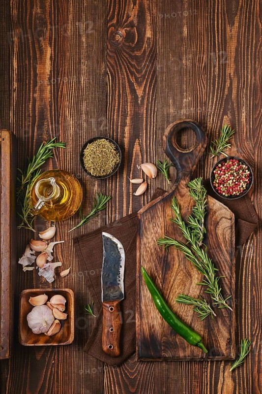 Overhead view of wooden cutting board with fresh rosemary and spices for piquant sauce or marinade on wooden kitchen table