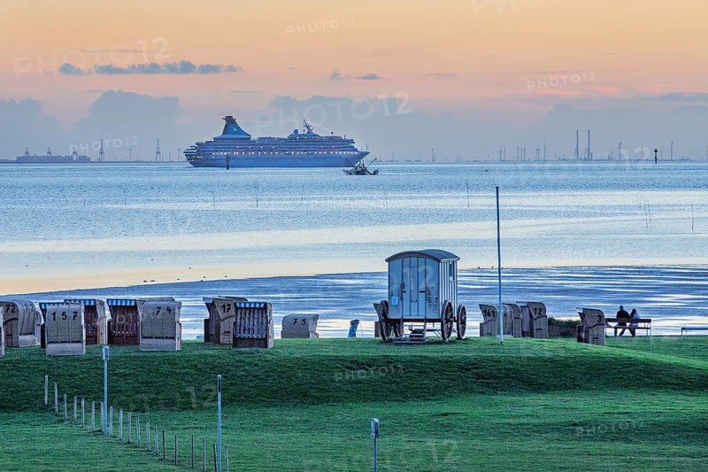Grassy beach with beach chairs and cruise ship Artania on the Weser at dusk