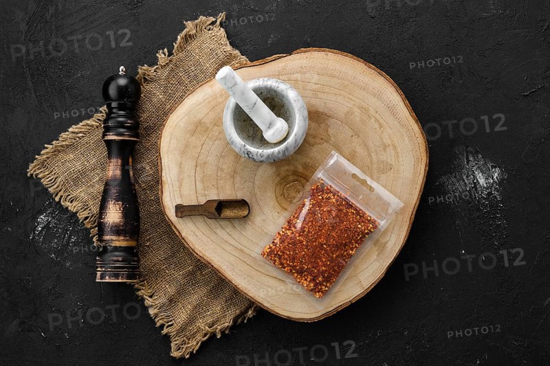 Wooden cross section with chili flakes in plastic package and stone mortar and mill
