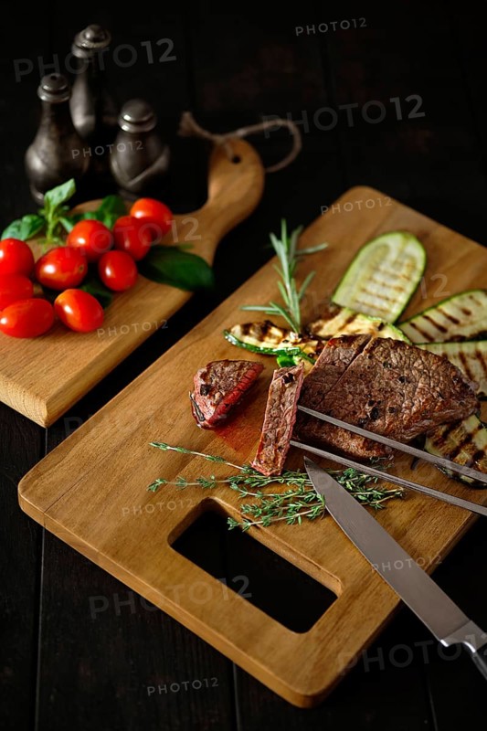 Low key photo of grilled beefsteak and zucchini on wooden cutting board
