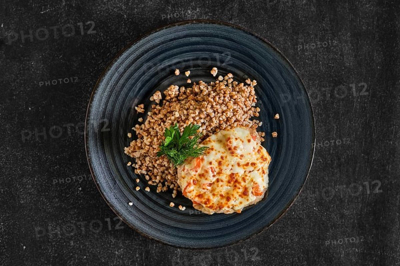 Top view of chopped pork meat baked with cheese and tomato served with buckwheat porridge